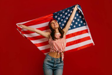 Mutlu genç hippi kadın kırmızı arka planda dururken Amerikan bayrağı taşıyor.