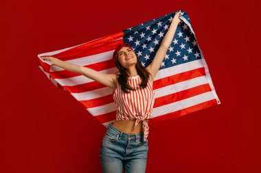 Mutlu genç hippi kadın kırmızı arka planda dururken Amerikan bayrağı taşıyor.