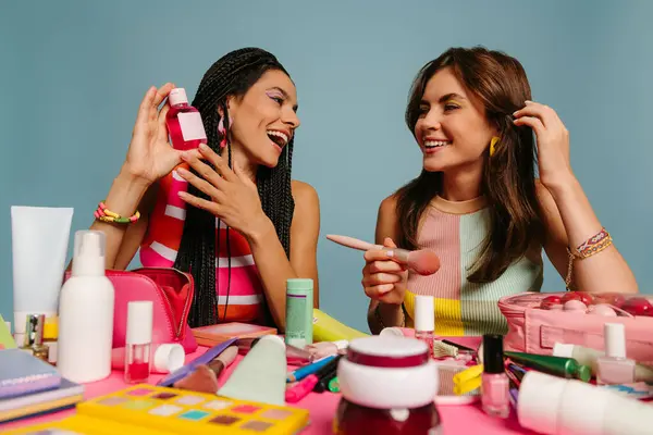 青い背景の机に座っている間 さまざまな美容製品を調べる2人の幸せな女性インフルエンサー — ストック写真