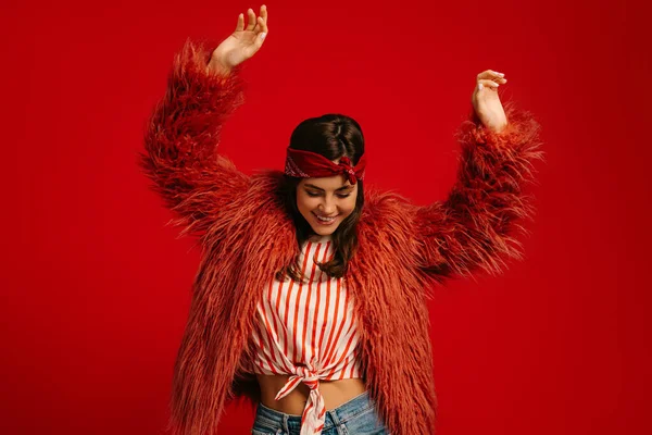 ふわふわのコートを着て赤い背景で踊るスタイリッシュな若いヒップスター女性 — ストック写真