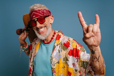 Hipster olgun bir adam şık, komik gömlekli, uzun tahtalı ve mavi arka planda jestler yapıyor.