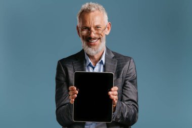 Mutlu yetişkin işadamı renkli arka planda dijital tabletinin dokunmatik ekranını gösteriyor
