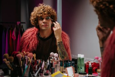 Sahne kostümlü kendine güvenen genç eşcinsel aynadaki yansımasına bakarak makyaj yapıyor.