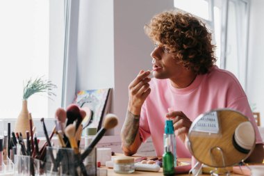 Kendine güvenen genç eşcinsel adam evde vakit geçirirken makyaj yapıyor.