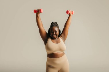 Spor kıyafetleri içinde kıvrımlı güzel bir Afrikalı kadın stüdyo arka planında egzersiz yaparken kendine güven yayıyor.