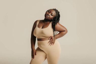 İç çamaşırlı güzel, kıvrımlı bir kadın stüdyo arka planında vücuduna güveniyor.