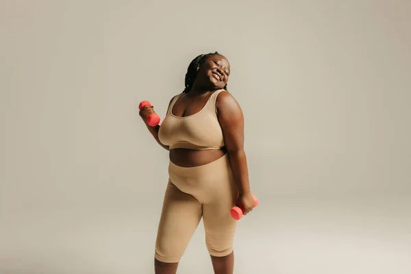在演播室背景下带哑铃进行运动服锻炼的自信加体形的非洲妇女 — 图库照片