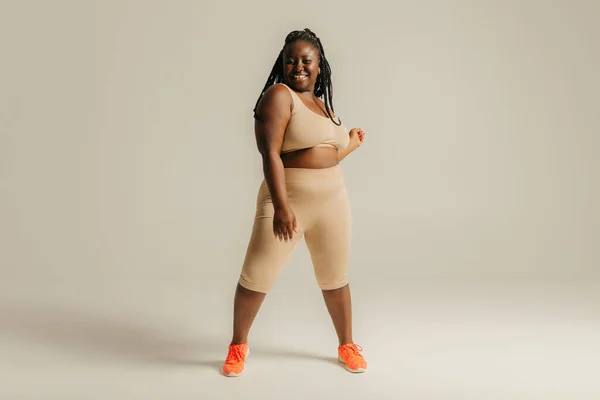 穿着运动服的快乐的卷曲的非洲女人 站在演播室的背景下 看上去对自己的身体充满信心 — 图库照片