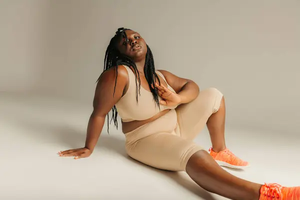 Beautiful plus size African woman in sportswear looking confident while sitting against studio background