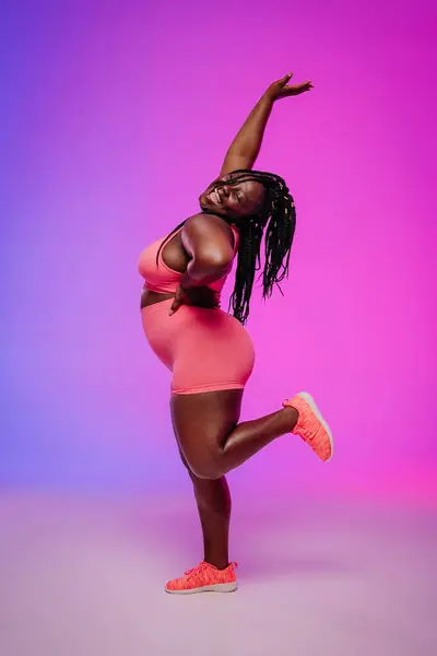 stock image Joyful African plus size woman in sportswear dancing and radiating self-love against colorful background
