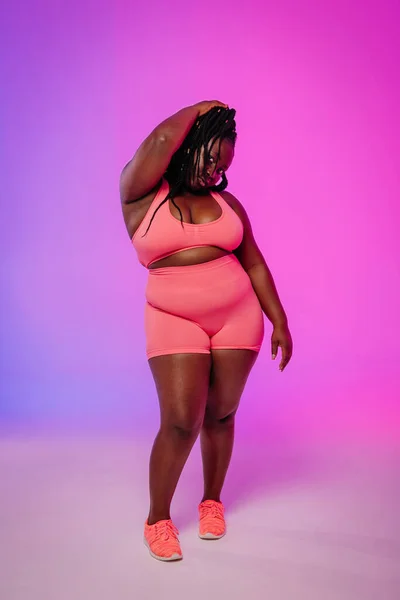 カラフルな背景に立っているスポーツウェアの自信を持ったアフリカ人プラスサイズの女性の全長 — ストック写真