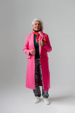 Şık giyinmiş, zarif, yaşlı bir kadın. Gri arka planda kendine güven ve sevgi yayıyor.