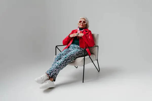 Δροσερή Ηλικιωμένη Γυναίκα Μοντέρνα Ρούχα Κάθεται Άνετη Καρέκλα Γκρι Φόντο — Φωτογραφία Αρχείου