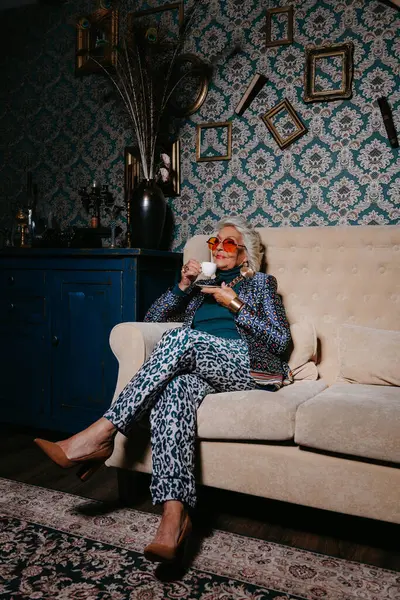 Элегантная Пожилая Женщина Модной Роскошной Одежде Наслаждаясь Кофе Сидя Диване — стоковое фото