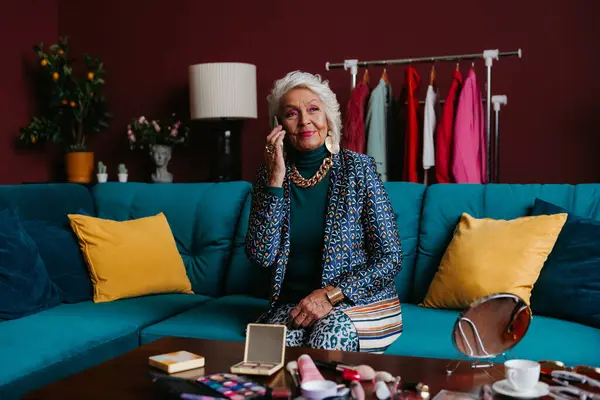 stock image Confident senior gray hair woman in fashionable wear talking on phone while sitting on the couch at home