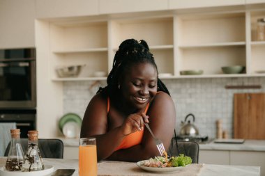 Güzel kıvrımlı Afrikalı kadın evde sağlıklı yemek yiyor.