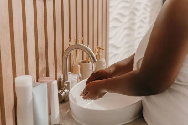 Close-up of plus size African woman covered in towel washing hands at the domestic bathroom
