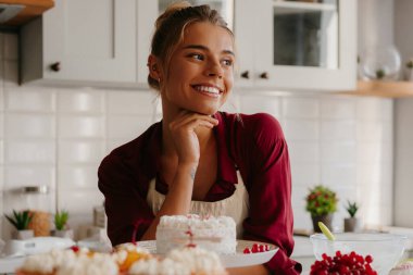 Genç bayan pastacı masaya tatlı yiyeceklerle yaslanırken yeni yaratıcı fikirler düşünüyor.