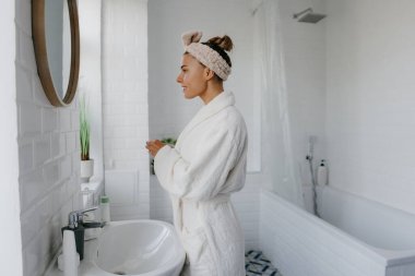 Bornozlu güzel bir kadın. Banyoda dururken aynaya bakıp gülümsüyor.