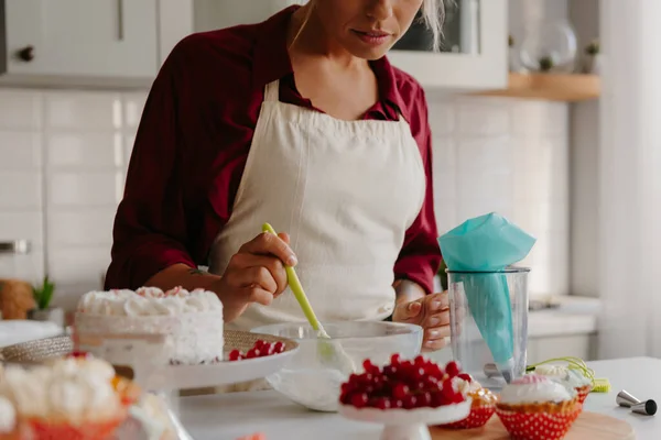 Close-up of young female pastry chef preparing whipped cream for cake at the domestic kitchen