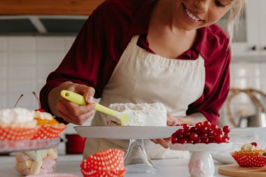 Ev mutfağında pasta yaparken krem şanti uygulayan kadın pasta şefinin yakın çekimi.