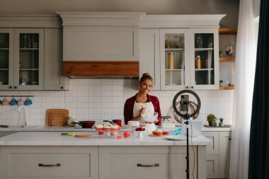 Güzel genç bir kadın ev yapımı pasta için krema hazırlıyor ve yemek blogu için video kaydediyor.