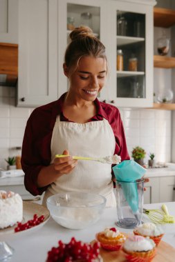 Gülümseyen genç bayan pasta şefi ev mutfağında pasta yaparken krem şanti hazırlıyor.