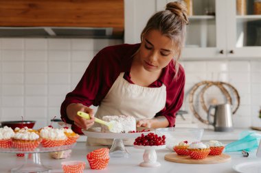 Ev mutfağında kek yaparken krem şanti uygulayan konsantre kadın pasta şefi.