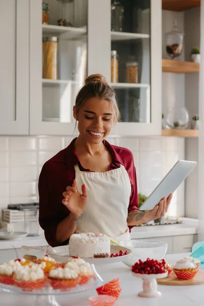 Confident female pastry chef using digital tablet while preparing cakes and muffins at the kitchen