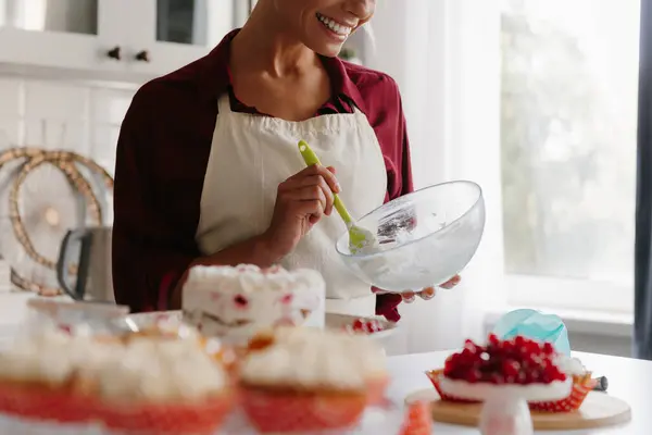Close-up of happy female pastry chef whisking whipped cream while making a cake at the kitchen