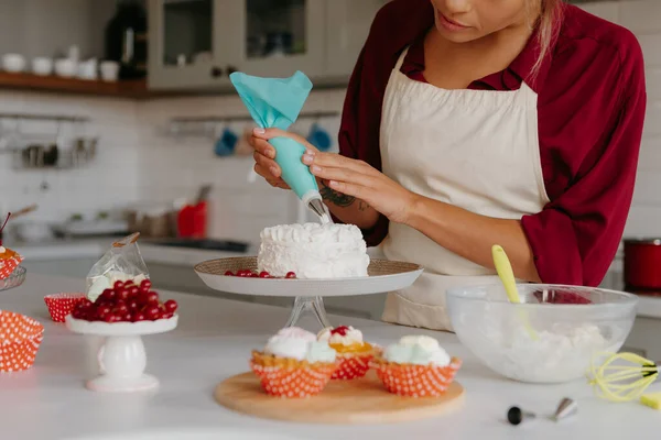 Close-up of skilled female pastry chef applying whipped cream while decorating cake at the kitchen