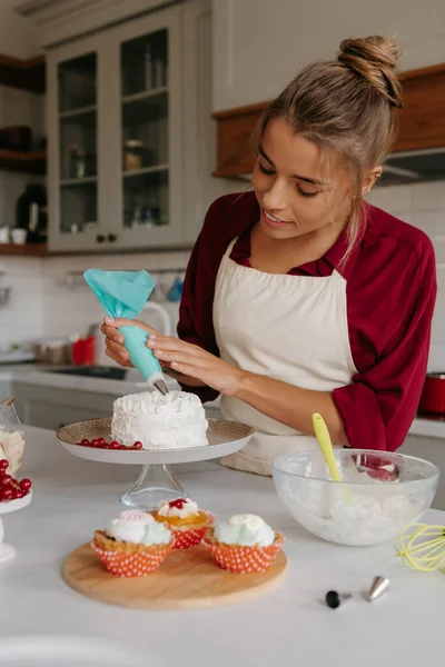 Confident female pastry chef applying whipped cream while decorating cake at the kitchen
