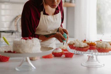 Mutfağa muffin koyarken krem şanti sıkan kadın şekerlemecinin yakın çekimi.