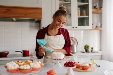 Neşeli kadın fırıncı mutfakta pasta süslerken krem şanti sürüyor.