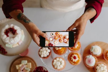 Kadın fırıncının masadaki tatlı yiyecekleri çekerken akıllı telefon kullanmasının en iyi görüntüsü.