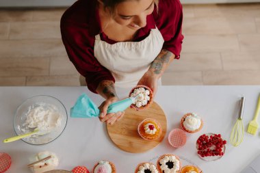 Mutfakta dururken krem şanti süren mutlu kadın şekerlemecinin üst görüntüsü.