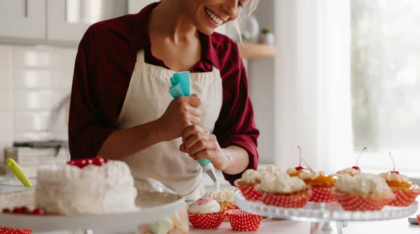 Close-up of female confectioner squeezing whipped cream while decorating muffins on the kitchen