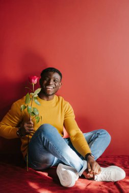 Kırmızı duvarın karşısında tek bir gül tutan mutlu genç Afrikalı adam.