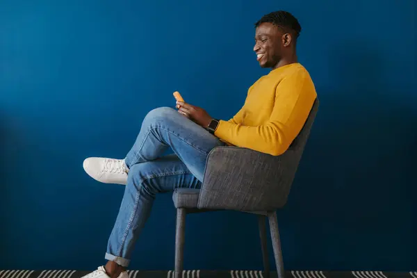 Щасливий Молодий Африканський Чоловік Повсякденному Одязі Використовуючи Смартфон Сидячи Стільці — стокове фото