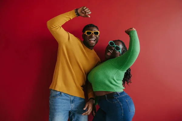 Fashionable young African couple in trendy glasses embracing and smiling on red background together
