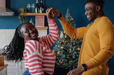 Mutlu genç Afrikalı çift evde birlikte yeni yılı kutlarken dans edip gülümsüyor.