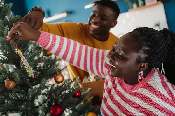 Beautiful young African couple enjoying fun time while decorating Christmas tree at home together