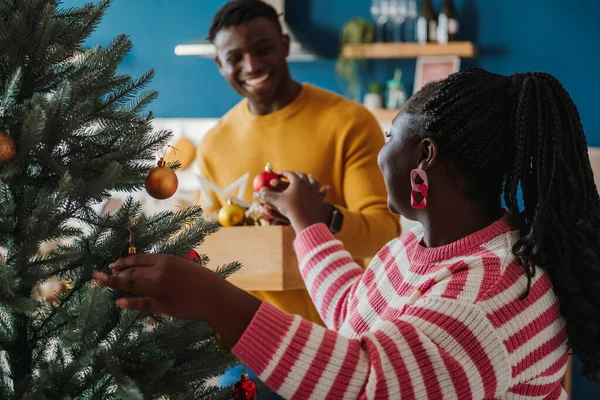 Joyful young African couple enjoying fun time while decorating Christmas tree at home together