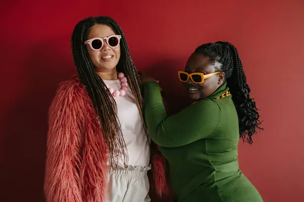 stock image Two fashionable plus size African woman with braided hair smiling while standing on red background together