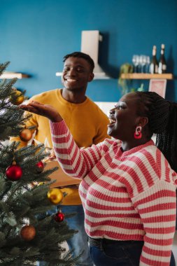 Neşeli genç Afrikalı çift evde Noel ağacını süslerken eğleniyor.