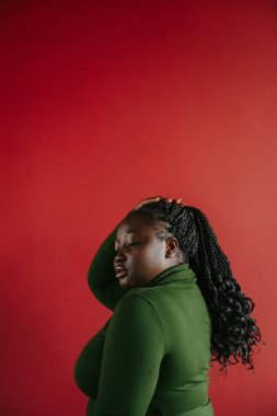Güzel kıvrımlı Afrikalı bir kadının kızıl arka planda örgülü saçlarına dokunuşunun yan görüntüsü.