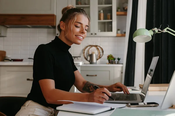 Smiling young woman making notes in her note pad while working at home