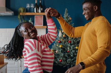 Mutlu genç Afrikalı çift evde birlikte yeni yılı kutlarken dans edip gülümsüyor.