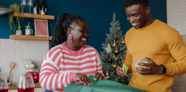 Güzel, genç Afrikalı çift mutlu görünüyor. Noel hediyelerini renkli kağıtlara sarıyorlar.