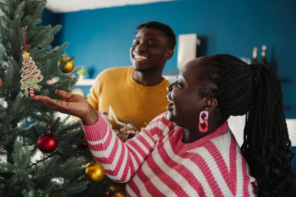 Joyful young African couple enjoying fun time while decorating Christmas tree at home together